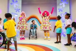 Fay cheering, arms oustretched, Fluffy cheering, beside a boy in a wheelchair, surrounded by children.